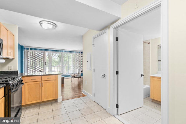 kitchen featuring dark countertops, light tile patterned floors, stainless steel microwave, and black range with gas stovetop