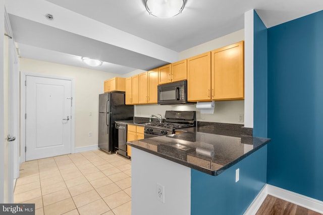 kitchen with light brown cabinets, black appliances, dark stone countertops, a peninsula, and baseboards