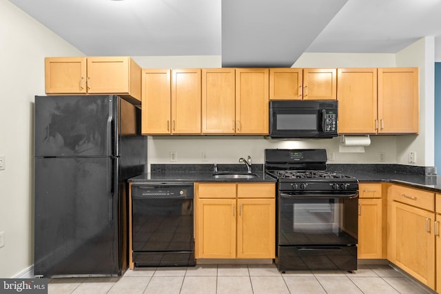 kitchen with dark stone counters, black appliances, light tile patterned floors, and a sink