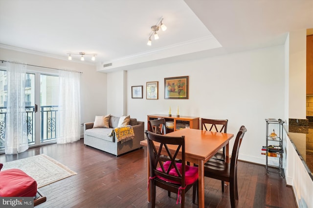 dining space with dark hardwood / wood-style flooring, rail lighting, a raised ceiling, and ornamental molding