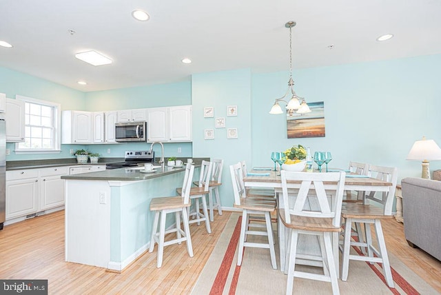 kitchen featuring white cabinets, light hardwood / wood-style floors, decorative light fixtures, stainless steel appliances, and a kitchen bar