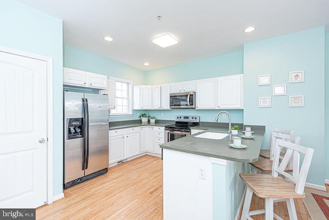 kitchen featuring sink, a breakfast bar area, white cabinetry, stainless steel appliances, and kitchen peninsula