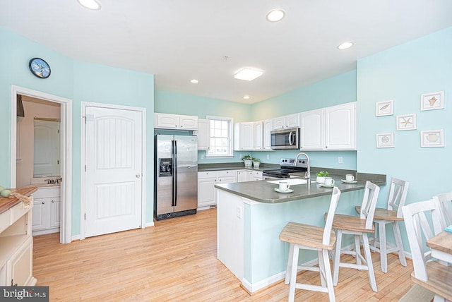 kitchen with white cabinets, kitchen peninsula, light hardwood / wood-style flooring, stainless steel appliances, and a breakfast bar area