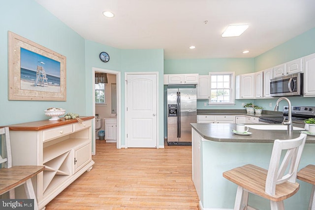 kitchen with white cabinets, stainless steel appliances, light hardwood / wood-style floors, and a breakfast bar