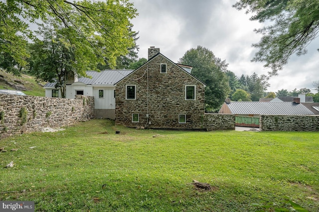 rear view of property featuring a standing seam roof, a lawn, a chimney, and metal roof