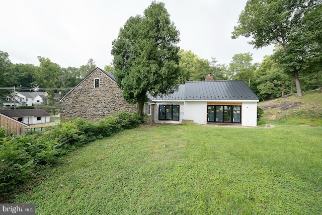 rear view of house with metal roof, a yard, a standing seam roof, and a chimney