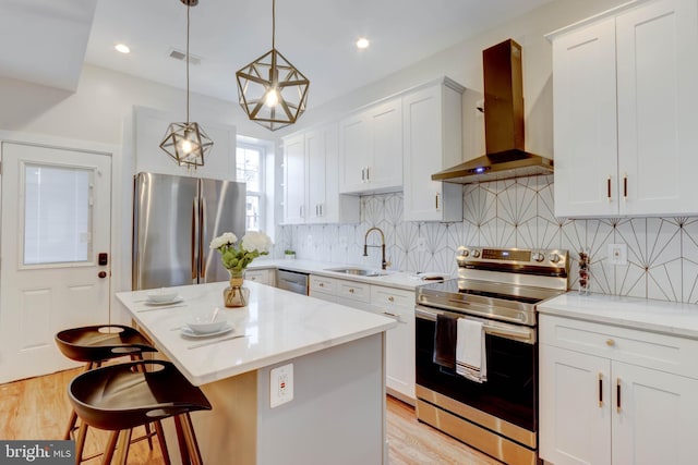 kitchen with appliances with stainless steel finishes, sink, a center island, decorative light fixtures, and wall chimney range hood