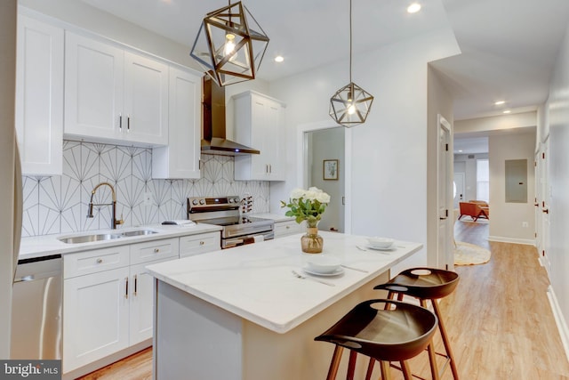 kitchen featuring white cabinetry, stainless steel appliances, sink, wall chimney range hood, and pendant lighting