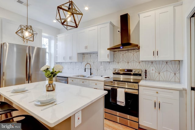 kitchen featuring sink, pendant lighting, a kitchen island, stainless steel appliances, and wall chimney exhaust hood