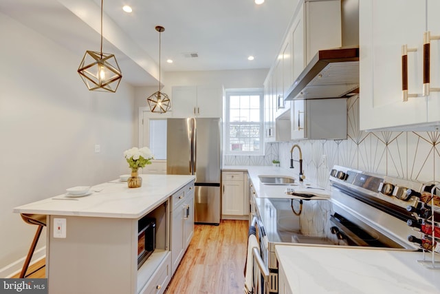 kitchen with appliances with stainless steel finishes, white cabinetry, sink, wall chimney range hood, and a center island