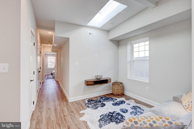 sitting room with beam ceiling, a healthy amount of sunlight, a skylight, and light wood-type flooring