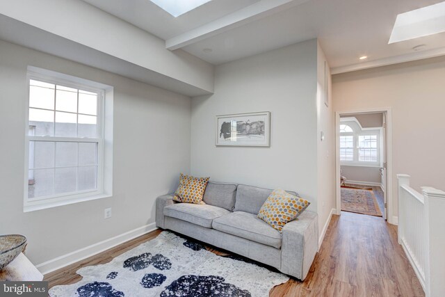 living room with beamed ceiling, a skylight, and light hardwood / wood-style floors