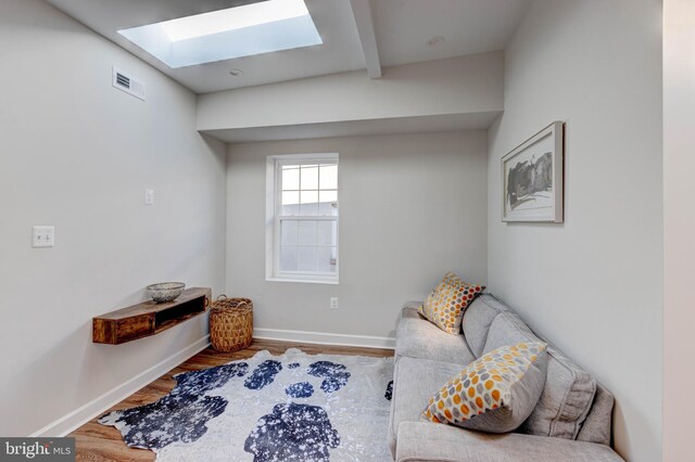 living area featuring hardwood / wood-style flooring, beam ceiling, and a skylight