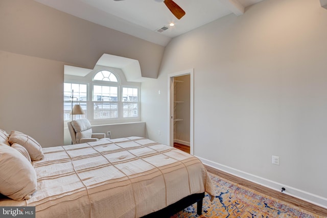 bedroom with ceiling fan, vaulted ceiling with beams, wood-type flooring, and a spacious closet