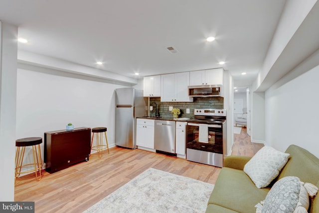 kitchen featuring white cabinets, decorative backsplash, light hardwood / wood-style flooring, and appliances with stainless steel finishes