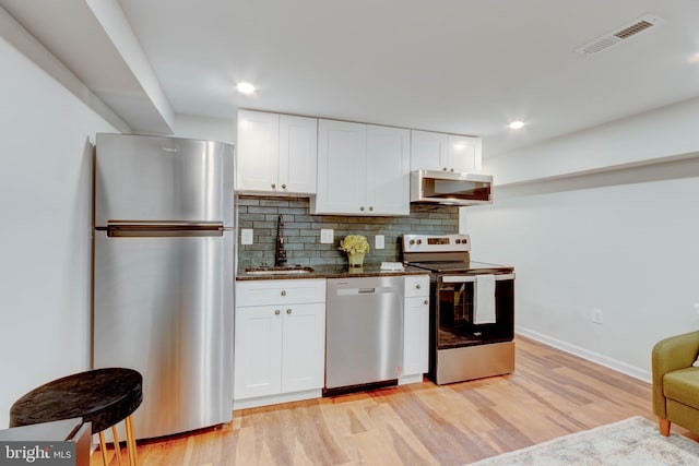 kitchen with dark stone countertops, white cabinetry, stainless steel appliances, ventilation hood, and tasteful backsplash