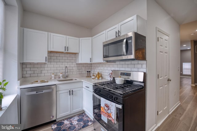 kitchen featuring sink, tasteful backsplash, stainless steel appliances, light hardwood / wood-style floors, and white cabinets