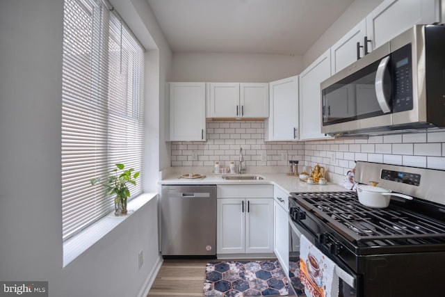 kitchen with appliances with stainless steel finishes, sink, white cabinets, and backsplash