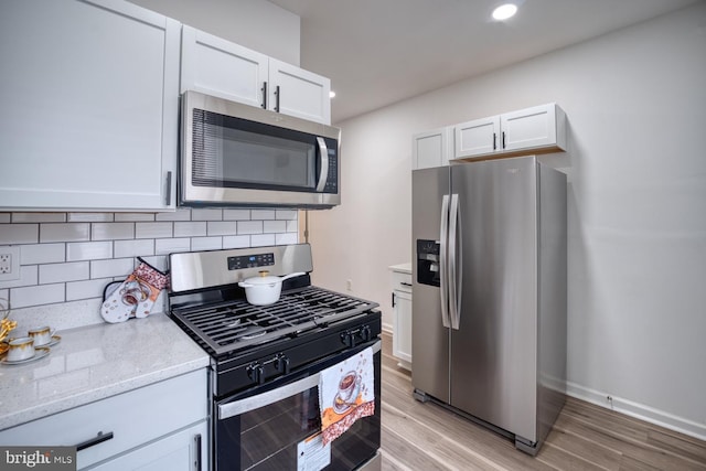 kitchen featuring tasteful backsplash, white cabinetry, stainless steel appliances, light stone countertops, and light hardwood / wood-style flooring