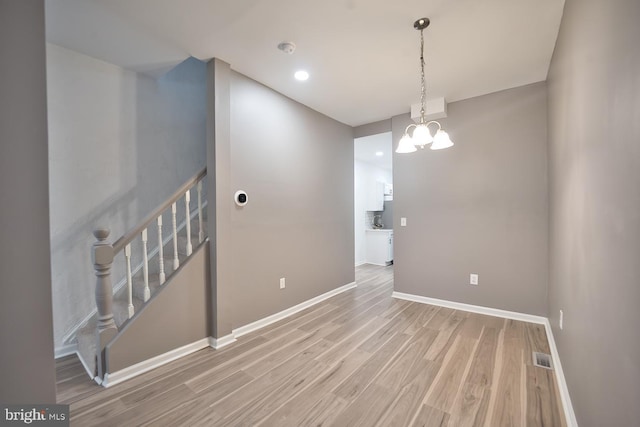 empty room with hardwood / wood-style flooring and an inviting chandelier