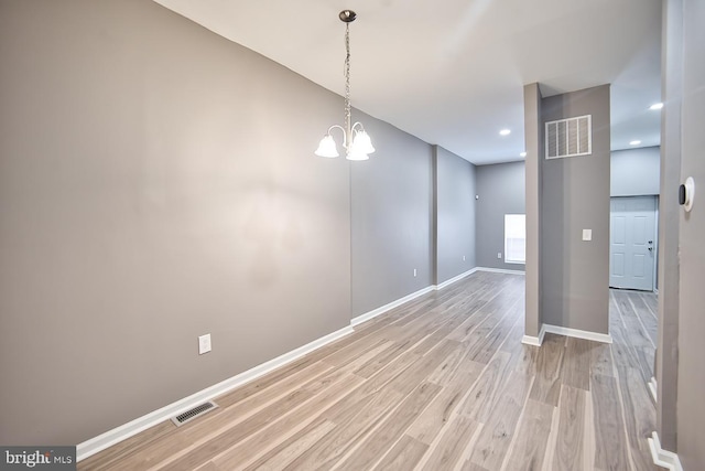 unfurnished room featuring an inviting chandelier and light wood-type flooring