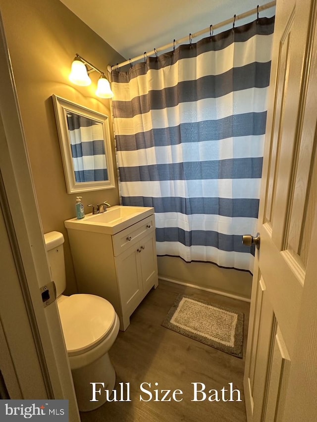 bathroom featuring toilet, wood finished floors, vanity, and shower / bath combination with curtain