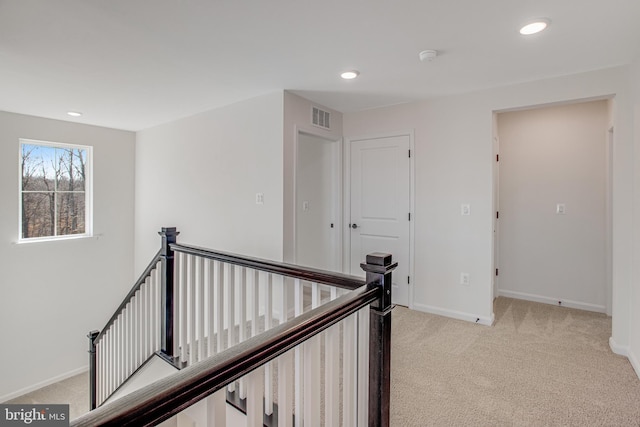 hall featuring light carpet, visible vents, baseboards, and an upstairs landing