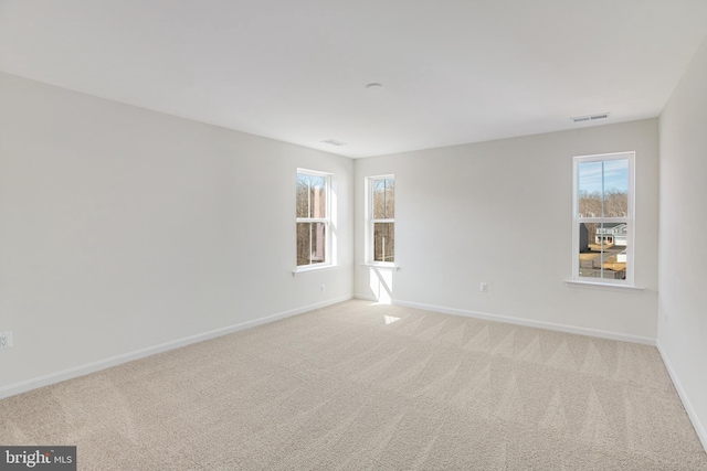 unfurnished room with baseboards, carpet, visible vents, and a wealth of natural light