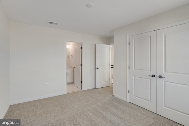 unfurnished bedroom with ensuite bathroom, carpet floors, visible vents, baseboards, and a closet