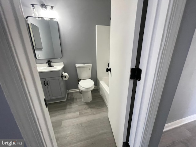 bathroom featuring hardwood / wood-style flooring, a tub to relax in, vanity, and toilet