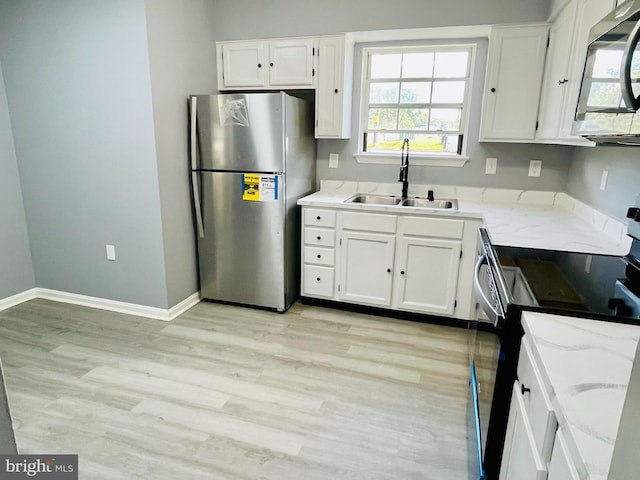 kitchen with white cabinets, sink, light hardwood / wood-style flooring, appliances with stainless steel finishes, and light stone countertops