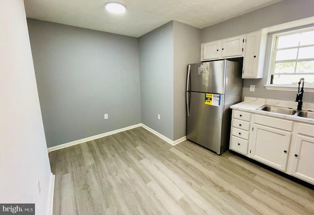 kitchen featuring light wood-type flooring, white cabinetry, stainless steel refrigerator, and sink