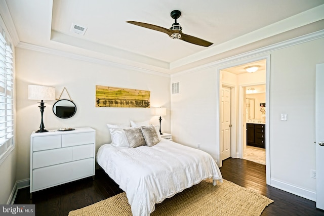 bedroom with crown molding, a tray ceiling, dark wood-type flooring, ceiling fan, and connected bathroom