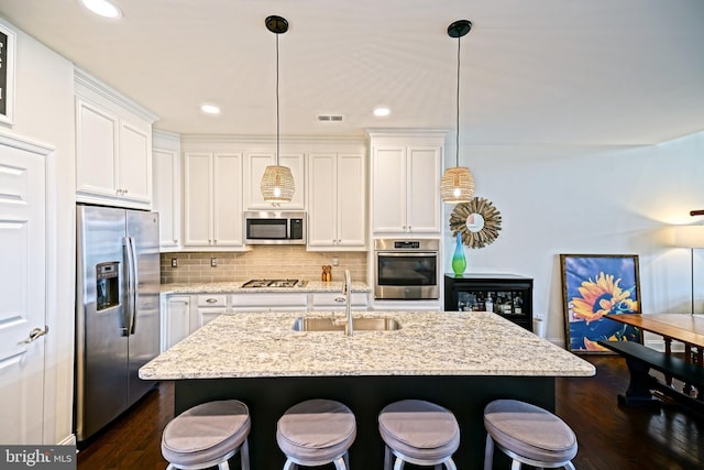 kitchen with appliances with stainless steel finishes, light stone countertops, sink, dark hardwood / wood-style floors, and an island with sink