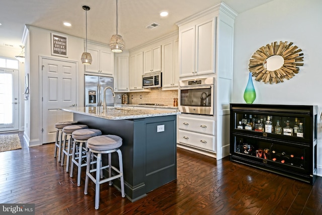 kitchen with dark hardwood / wood-style flooring, appliances with stainless steel finishes, an island with sink, a kitchen bar, and white cabinets