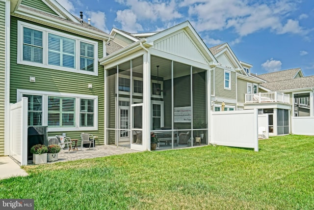 rear view of property featuring a lawn, a patio, and a sunroom