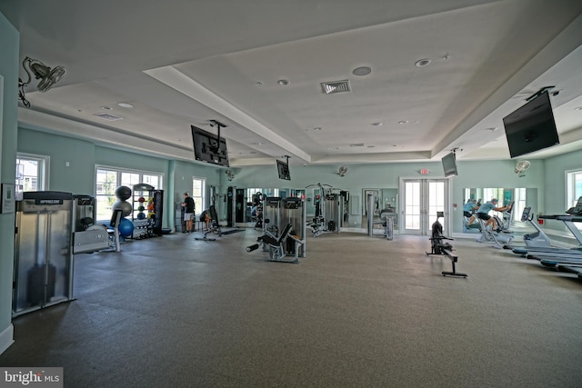 gym featuring plenty of natural light, a raised ceiling, and french doors