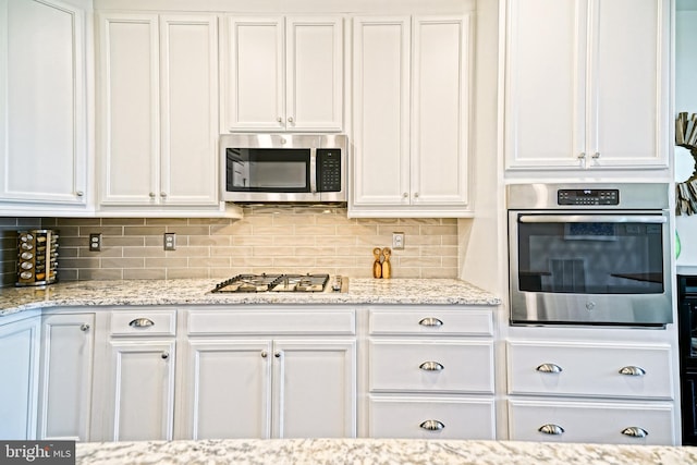 kitchen featuring light stone counters, stainless steel appliances, decorative backsplash, and white cabinetry