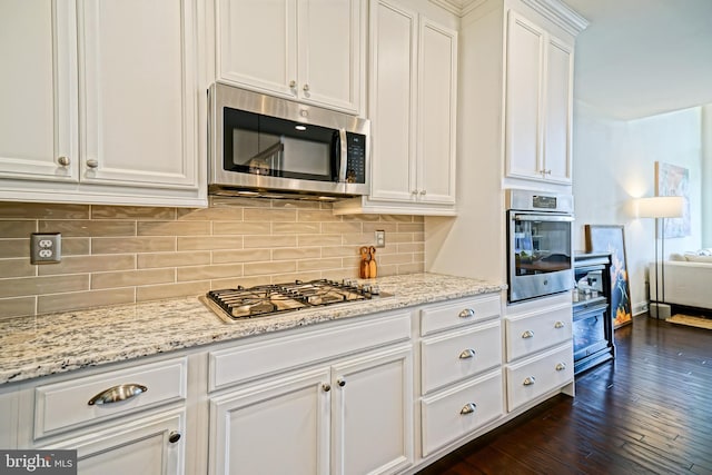 kitchen with white cabinets, appliances with stainless steel finishes, light stone counters, and dark hardwood / wood-style floors