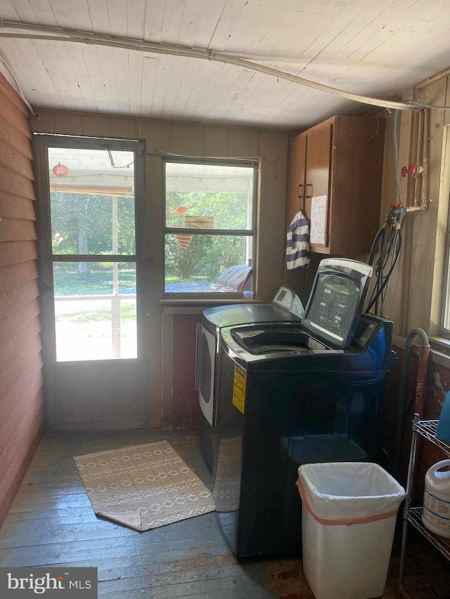 clothes washing area with hardwood / wood-style floors, a wealth of natural light, independent washer and dryer, and wood walls