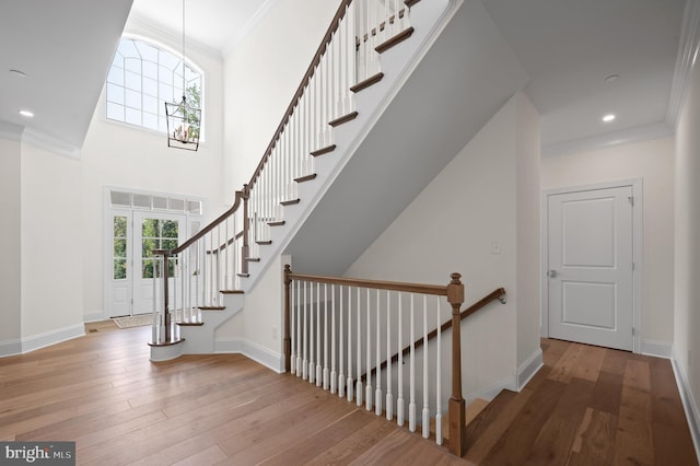 stairs with ornamental molding, a high ceiling, and wood-type flooring