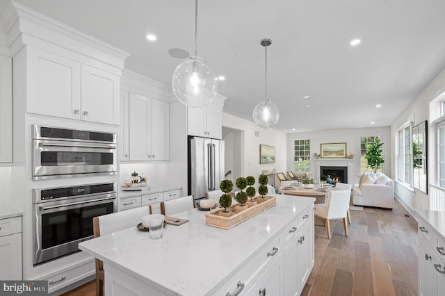 kitchen with a kitchen island, white cabinetry, stainless steel appliances, decorative light fixtures, and hardwood / wood-style flooring