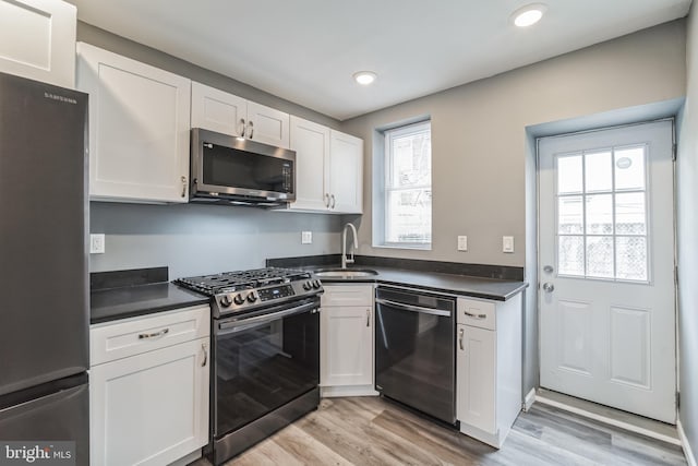 kitchen with stainless steel appliances, sink, white cabinets, and light hardwood / wood-style flooring