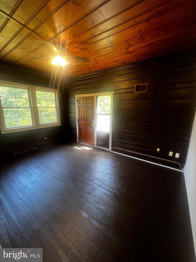 empty room with a healthy amount of sunlight, dark wood-type flooring, and wood ceiling