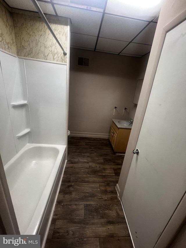 full bathroom with hardwood / wood-style flooring, washtub / shower combination, toilet, vanity, and a drop ceiling