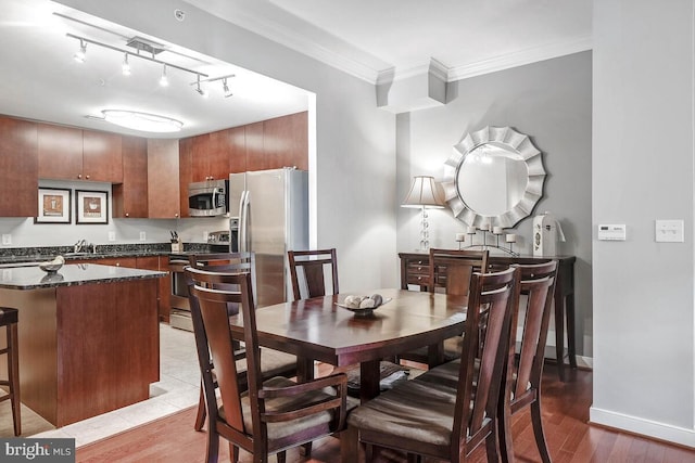 dining space featuring light wood finished floors, track lighting, baseboards, and crown molding