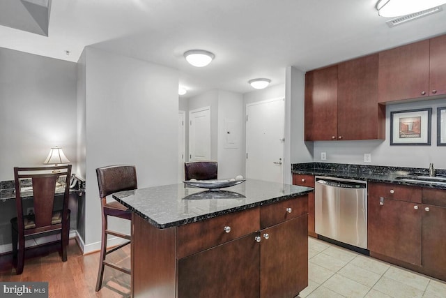 kitchen featuring a sink, visible vents, stainless steel dishwasher, a center island, and dark stone countertops