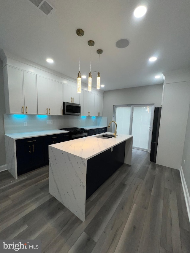 kitchen featuring hanging light fixtures, a center island with sink, sink, white cabinetry, and dark hardwood / wood-style flooring