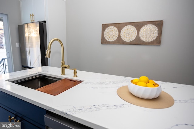 details with sink, blue cabinetry, stainless steel refrigerator, white cabinetry, and light stone counters