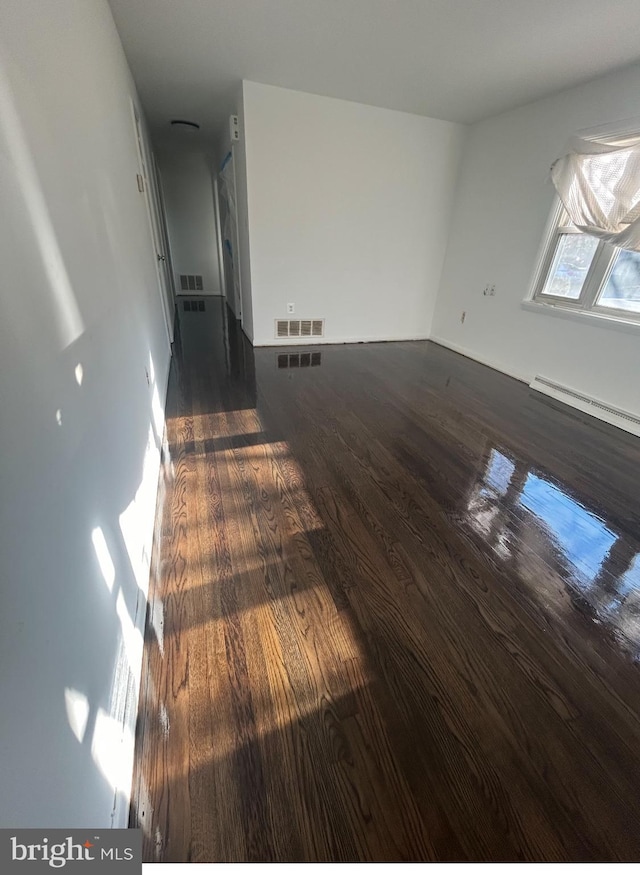 spare room featuring a baseboard heating unit and dark wood-type flooring